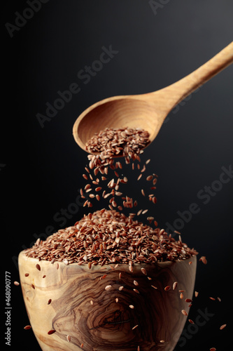 Grains of flaxseed are poured into the wooden bowl. photo