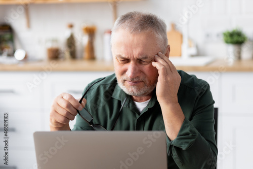 Elderly man suffering from severe headache while working on laptop
