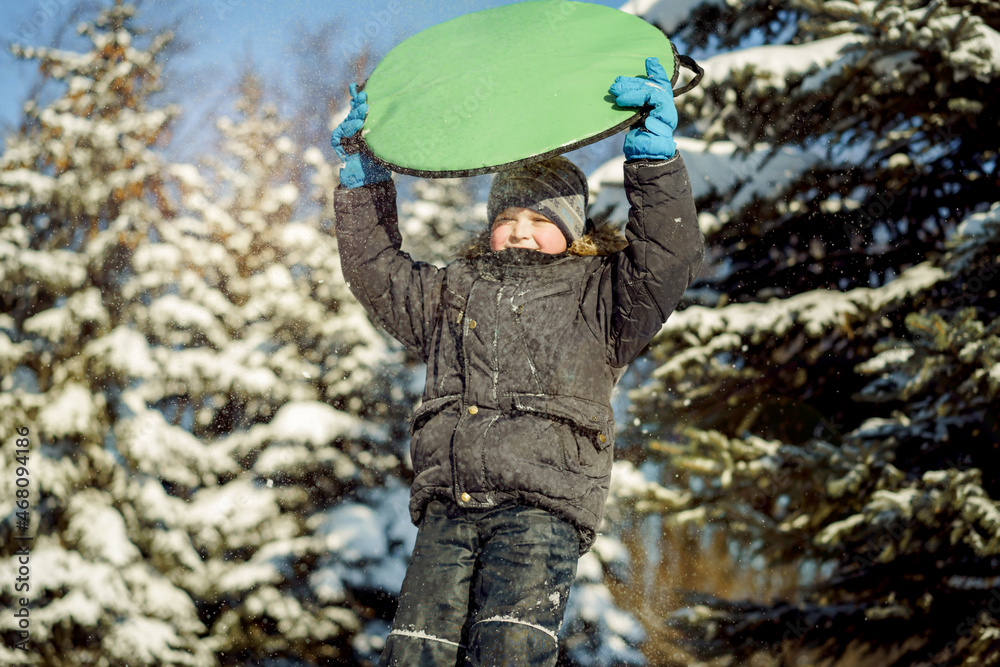 cute caucasian boy holding a snow saucer to slide from hill in winter park
