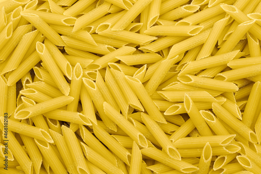 Dry uncooked penne pasta background, top view.