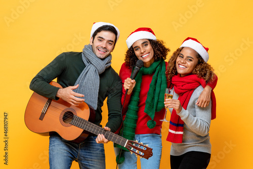 Multiethnic group of close friends having party singing and celebrating Christmas in yellow studio isolated background