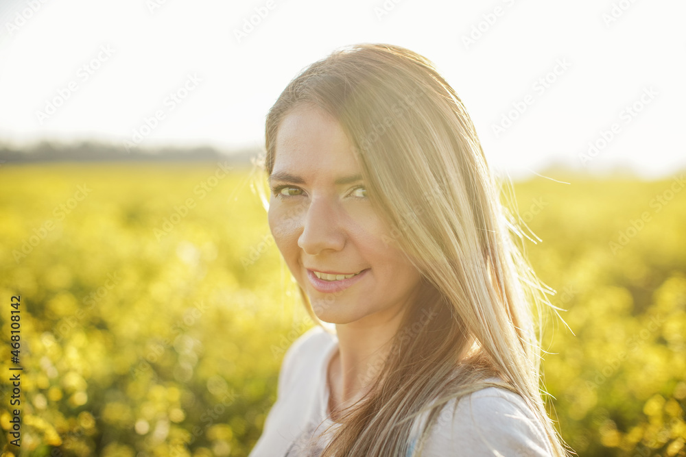 Portrait of young woman with long hair, yellow flower field and sun backlight behind her Portrait of young woman with long hair, yellow flower field and sun backlight behind her