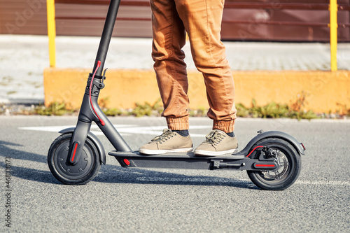 Young man in casual trousers riding an electric scooter detail on his feet and wheel over asphalt road