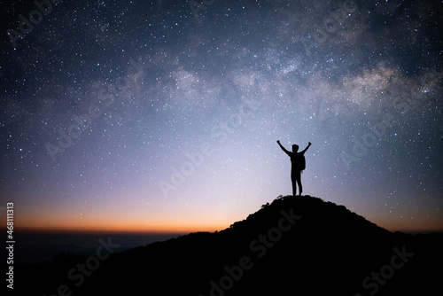 Silhouette of young traveler and backpacker standing and open arm and watched the star and milky way alone on top of the mountain. He enjoyed traveling and was successful when he reached the summit.