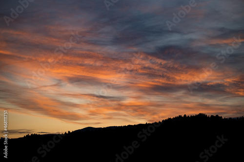 Brennender Himmel mit rot orangen Wolken und Sonnenuntergang mit Bergpanorama als Scherenschnitt im Vordergrung