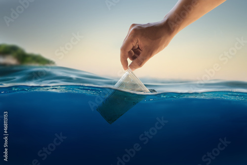 Hand of volunteer cleaning a plastic up floating in ocean. Plastic pollution in ocean and sea concept.
