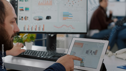 Paralysed business man sitting immobilized in wheelchair working at tablet and computer in same time analysing financial graphs, pc showing data prosessing on display for project regarding economy