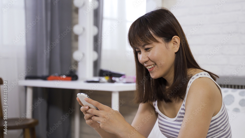 portrait asian chinese teenage girl chuckling, having fun playing mobile game at home while sitting in bed in the morning portrait asian chinese teenage girl chuckling, having fun playing mobile game at home while sitting in bed in the morning