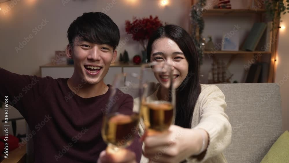 Virtual Party Concept. Smiling asian couple sitting on sofa and face camera having online video call with friends. slow motion boy and girl drinking wine and toasting celebrating together at home Virtual Party Concept. Smiling asian couple sitting on sofa and face camera having online video call with friends. slow motion boy and girl drinking wine and toasting celebrating together at home
