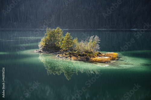 Eine kleine Insel mit Bäumen in einem Bergsee mit grün türkisem Wasser und kompletter Spiegelung auf der Wasseroberfläche. Eibsee, Deutschland.