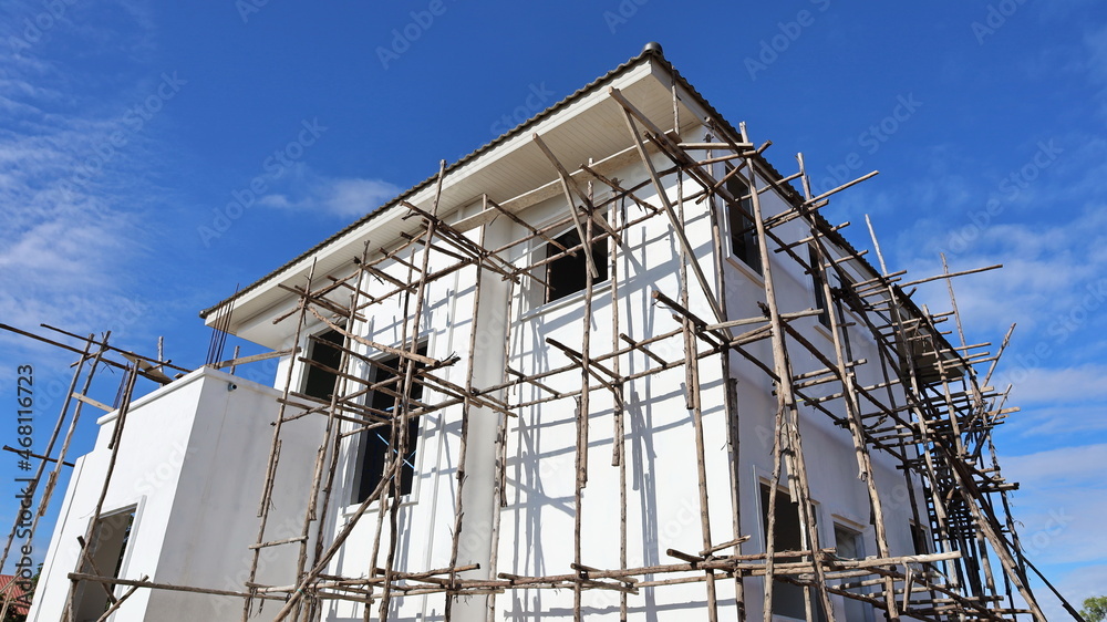 Construction of houses and wooden scaffolding. White modern single house under construction in bottom view on blue sky background. selective focus