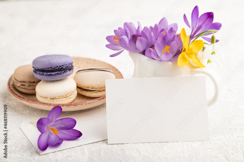 White paper business card mockup with spring snowdrop crocus flowers and multicolored macaroons on gray concrete background. side view, copy space.