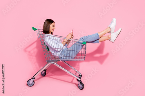 Photo of shiny cute young woman wear white sweater sitting shopping cart chattin Fotobehang