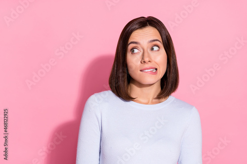 Photo of pretty doubtful young lady dressed white jumper biting lip looking empty space isolated pink color background