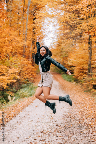 Cute girl smiling  jumping and playing with the leaves in the woods during the autumn season.