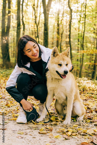 Portrait of a happy girl walking her pet dog in the forest during the autumn. Life of Akita inu breed.