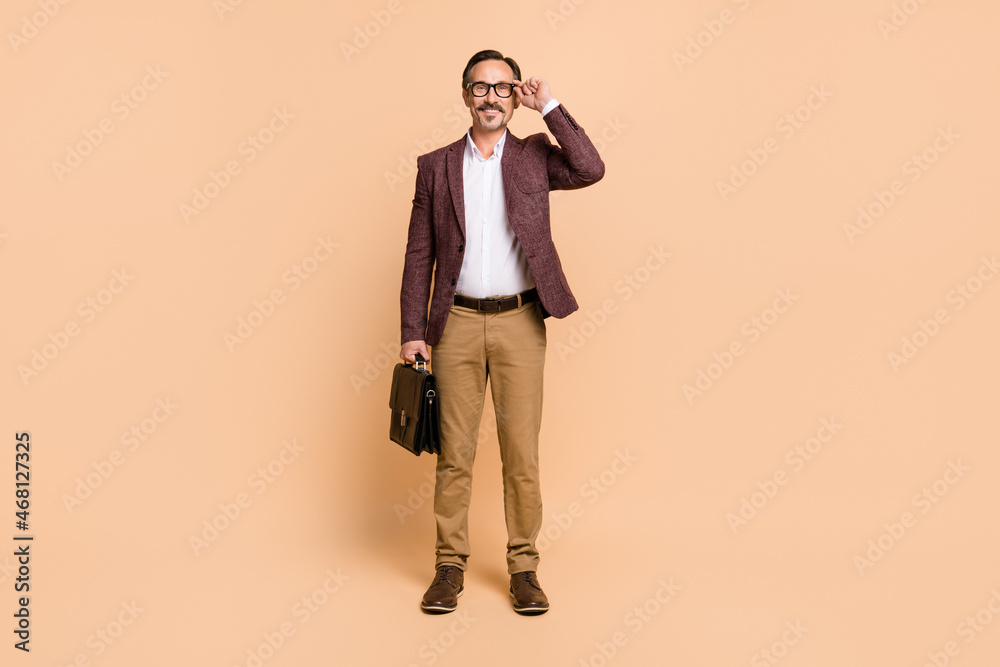 Full length body size view of attractive imposing cheery man director touching specs isolated over beige color background Full length body size view of attractive imposing cheery man director touching specs isolated over beige color background