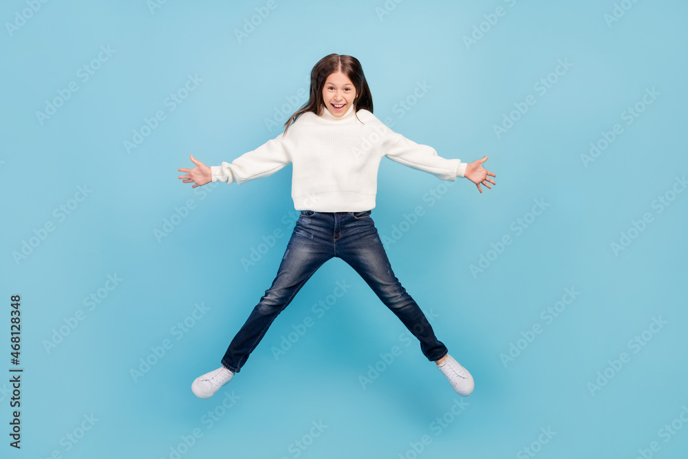Photo of pretty excited student girl wear white sweater smiling jumping high like star isolated blue color background Photo of pretty excited student girl wear white sweater smiling jumping high like star isolated blue color background