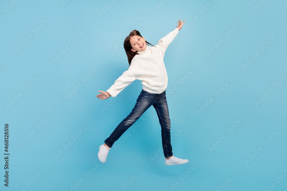 Obraz premium Photo of excited sweet preteen girl dressed white pullover jumping high arms sides smiling isolated blue color background