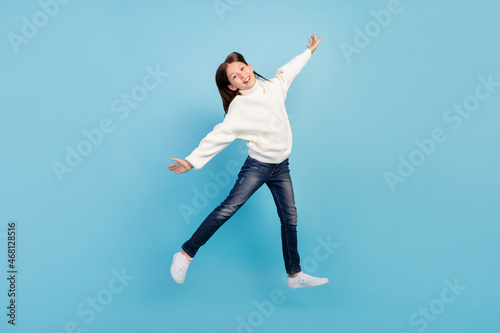 Photo of excited sweet preteen girl dressed white pullover jumping high arms sides smiling isolated blue color background