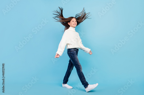 Photo of sweet shiny preteen girl dressed white pullover walking air blowing looking empty space smiling isolated blue color background