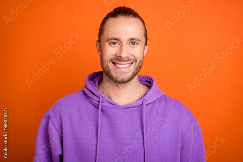 Photo of optimistic millennial brown tail hairdo guy wear purple hoodie isolated on orange color background photo