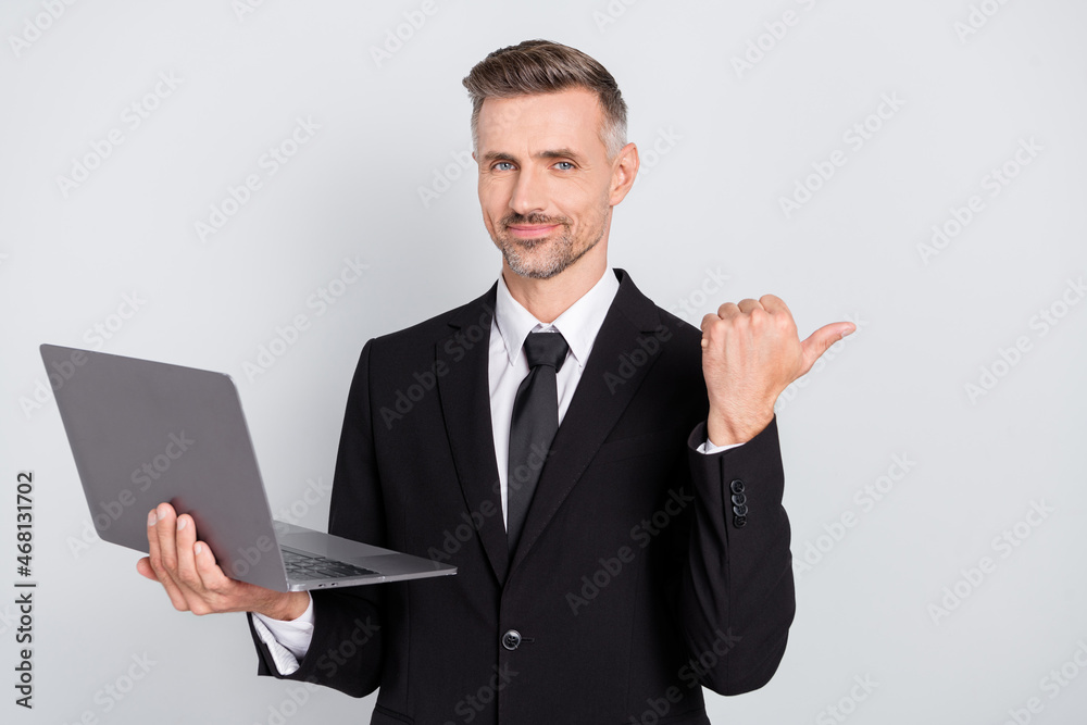 Photo of pretty handsome mature advisor dressed black suit holding modern gadget pointing thumb empty space isolated grey color background Photo of pretty handsome mature advisor dressed black suit holding modern gadget pointing thumb empty space isolated grey color background
