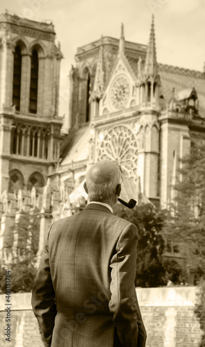 Old gentleman (unrecognizable; back view) with pipe looking on Notre Dame cathedral. Paris, France. Thinking about time, life, god. Sepia historic photo
