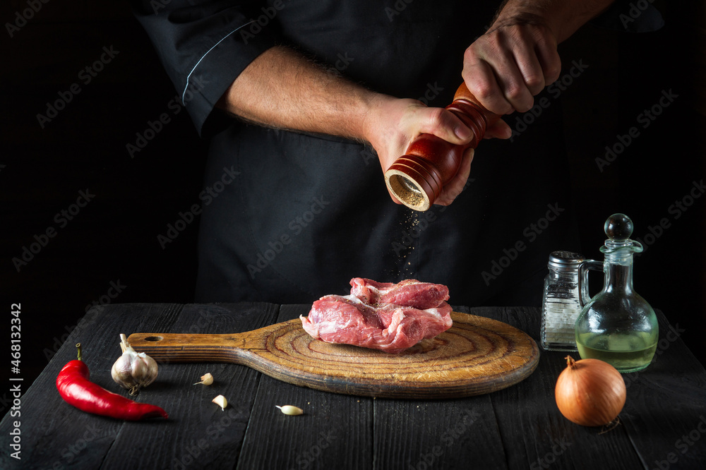 Cook cooking raw meat fillet and adding pepper or chili for marinade. Working environment in kitchen in restaurant or cafe