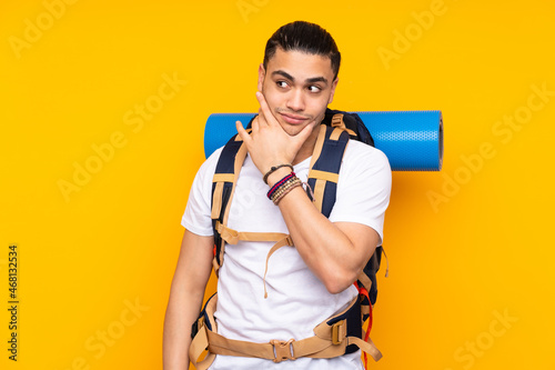 Young mountaineer asian man with a big backpack isolated on yellow background thinking an idea