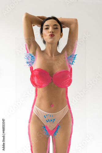Woman sending air kiss to camera while posing over creative glass with unshaven armpits