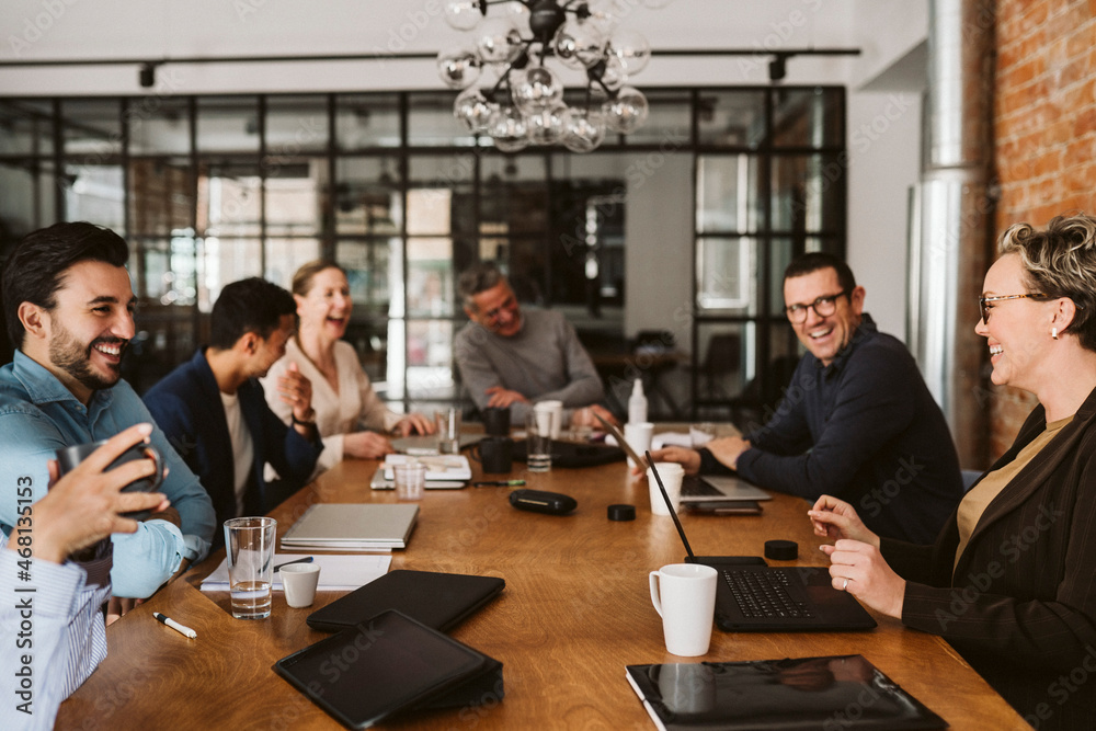 Cheerful business professionals laughing while sitting at conference table in board room Cheerful business professionals laughing while sitting at conference table in board room