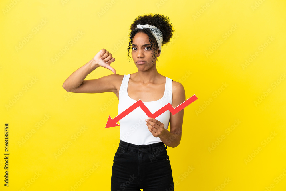 Young african american woman isolated on yellow background holding a downward arrow and doing bad signal