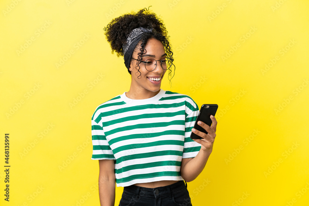 Young african american woman isolated on yellow background sending a message or email with the mobile Young african american woman isolated on yellow background sending a message or email with the mobile