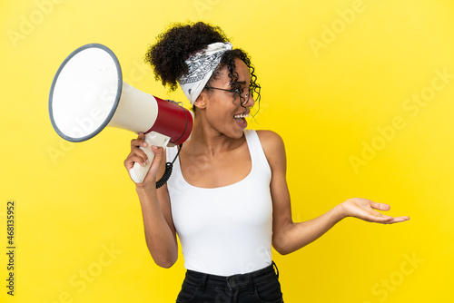 Young african american woman isolated on yellow background holding a megaphone and with surprise facial expression © luismolinero