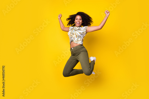 Full body photo of young afro girl celebrate victory rejoice victory fists hands air jump isolated over yellow color background