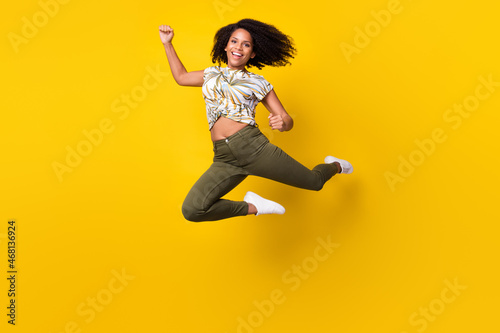 Full size photo of young excited african girl rejoice winner success jump isolated over yellow color background