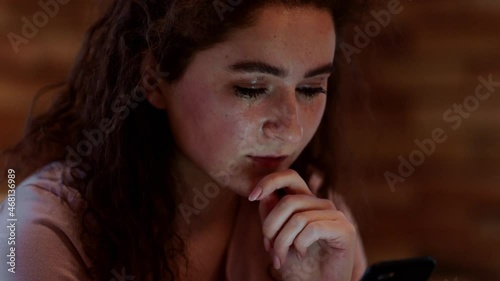 Closeup to the camera depressed girl crying in her bedroom she holding a smartphone in hands photo