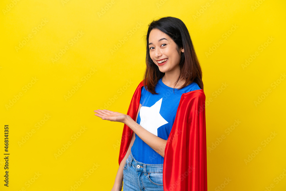 Super hero Vietnamese woman isolated on yellow background presenting an idea while looking smiling towards Super hero Vietnamese woman isolated on yellow background presenting an idea while looking smiling towards