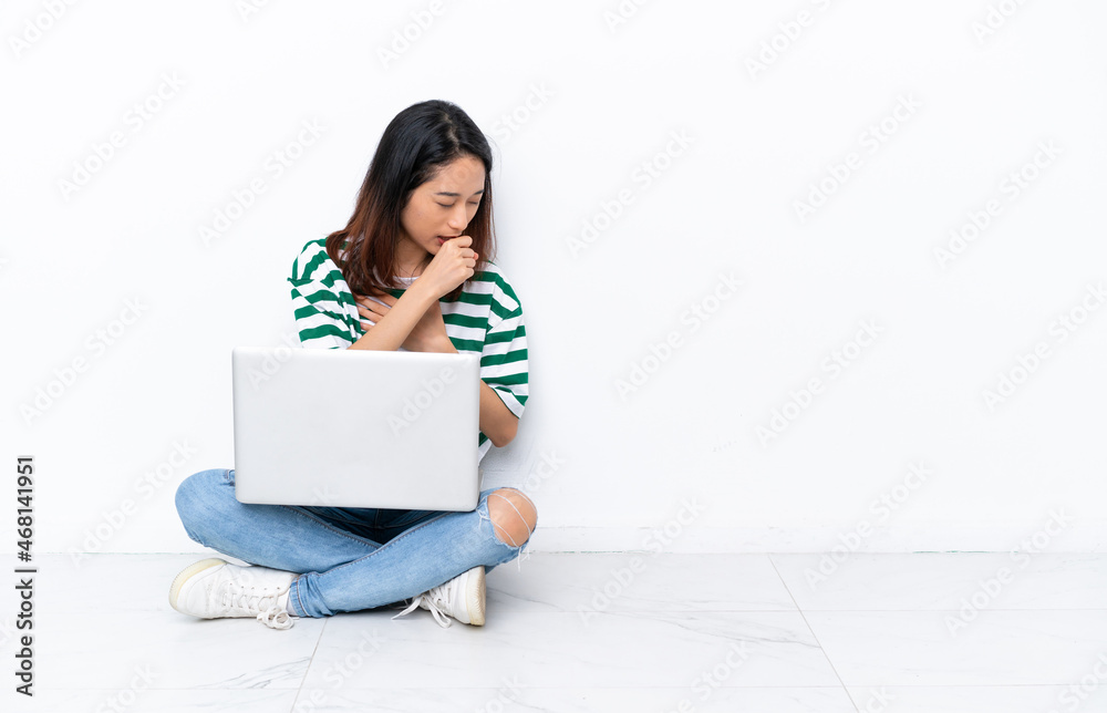 Young Vietnamese woman with a laptop sitting on the floor isolated on white wall is suffering with cough and feeling bad Young Vietnamese woman with a laptop sitting on the floor isolated on white wall is suffering with cough and feeling bad