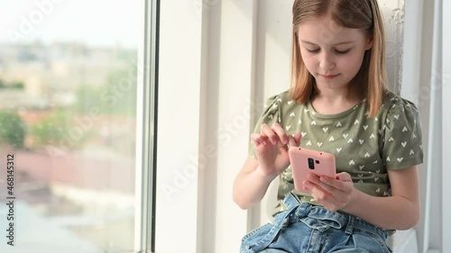 Preteen girl with smartphone sitting at home and looking social media, typing. Cute female kid with cell phone indoor