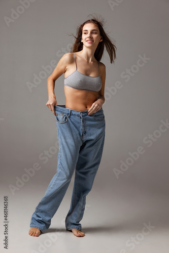 Portrait of young beautiful slim girl in blue jeans jumpersuit posing isolated over gray studio background. Weight Loss concept.