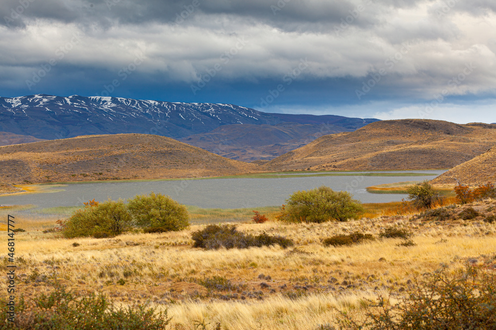 Autumn in Patagonia: landscape with rolling hills, mountains and a lake under overcast sky