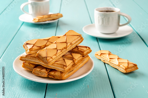 Italian crispy bakery Sfogliatine glassate on a white saucer and two cups of hot coffee over turquoise wooden table. Sweet breakfast with apricot glase puff pastries and freshly brewed coffee. photo