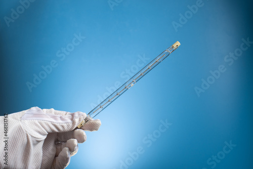 Linear halogen lamp with double base R7S. A gloved hand holds a lamp on a blue background. photo