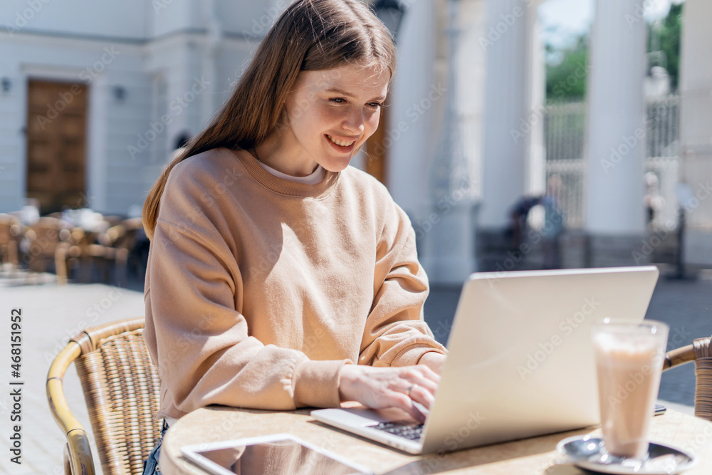 Online training. A teenager communicates with friends on a social network. The blogger writes a message to the mail. Sitting in a summer cafe on the street. A woman uses a laptop.