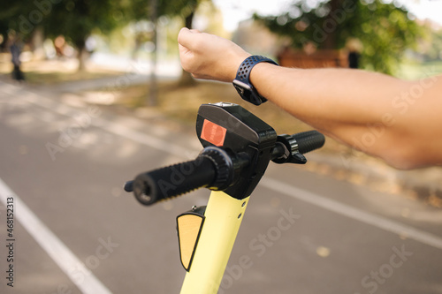 Fototapeta Naklejka Na Ścianę i Meble -  Hand of man connect an electric scooter outdoors. Woman using smart watch for contactless payment. Ecological transportation concept