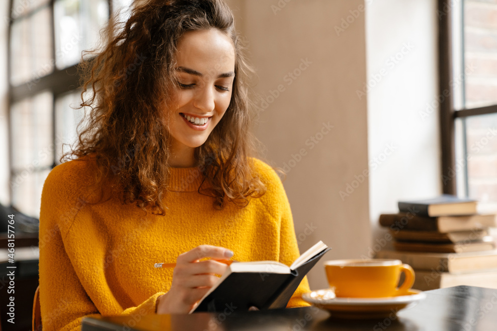 Young white woman writing down notes while drinking coffee