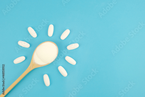 Hydrolyzed Marine Collagen Powder in wooden spoon and Vitamins in white tablets on blue background. Banner about health, taking vitamins. Creative background about drugs and food supplements. Top view