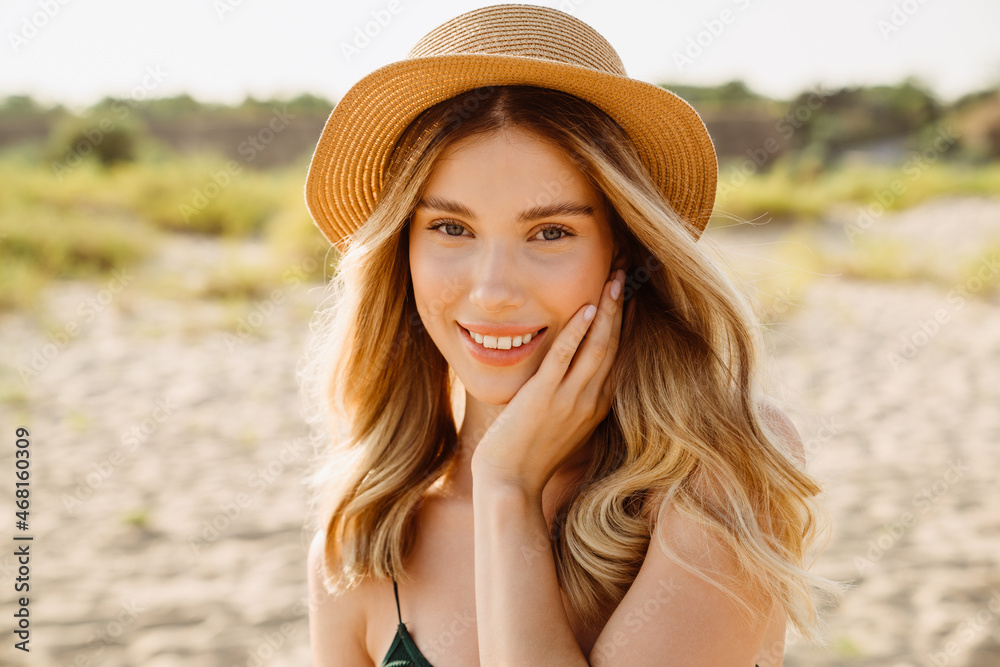 Young blonde woman wearing straw hat smiling and looking at camera